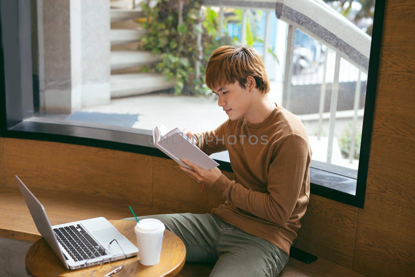 Handsome asian man using laptop sitting on wooden table in coffee shop with a cup of coffee by makidotvn