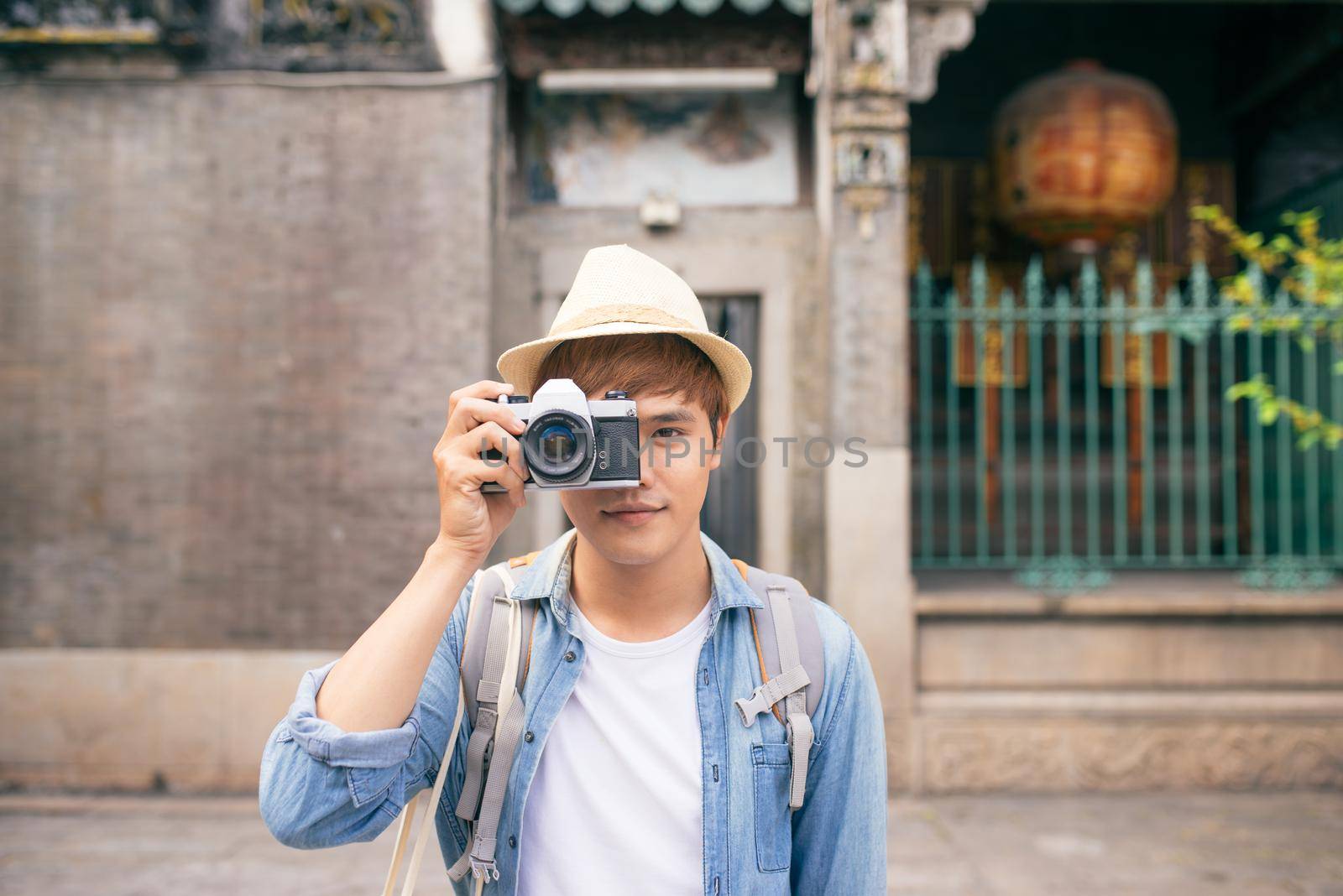 Hobby and travel. Young man with backpack taking photo with his camera on asian street.