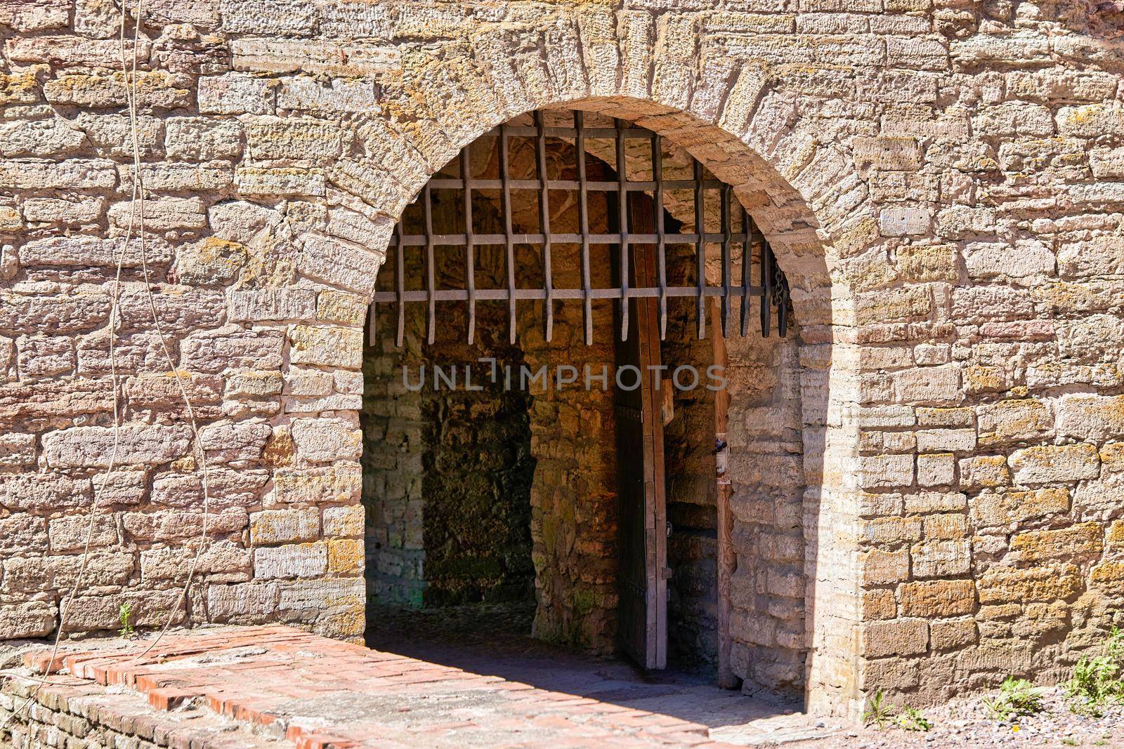 A gate with a thick metal lattice covering the entrance to the fortress. Red brick fortress wall with gates