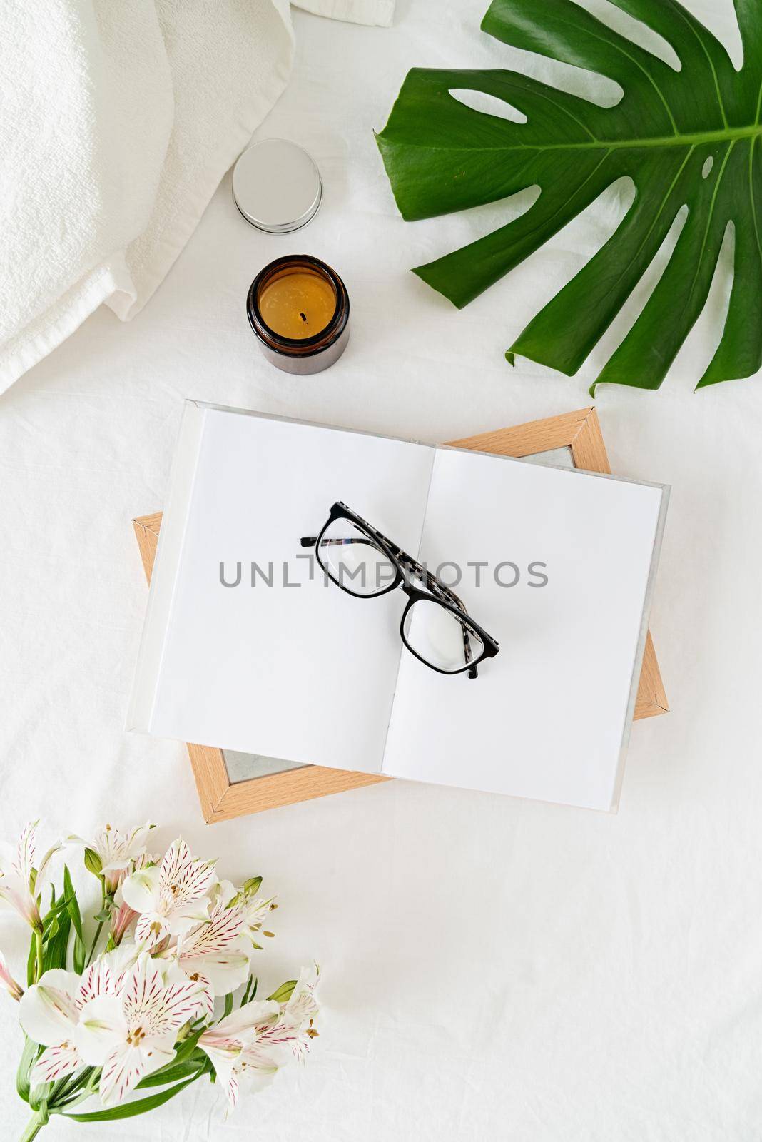 Blank opened book, candle, glasses, flowers on white bed, flat lay, mock up, flat lay