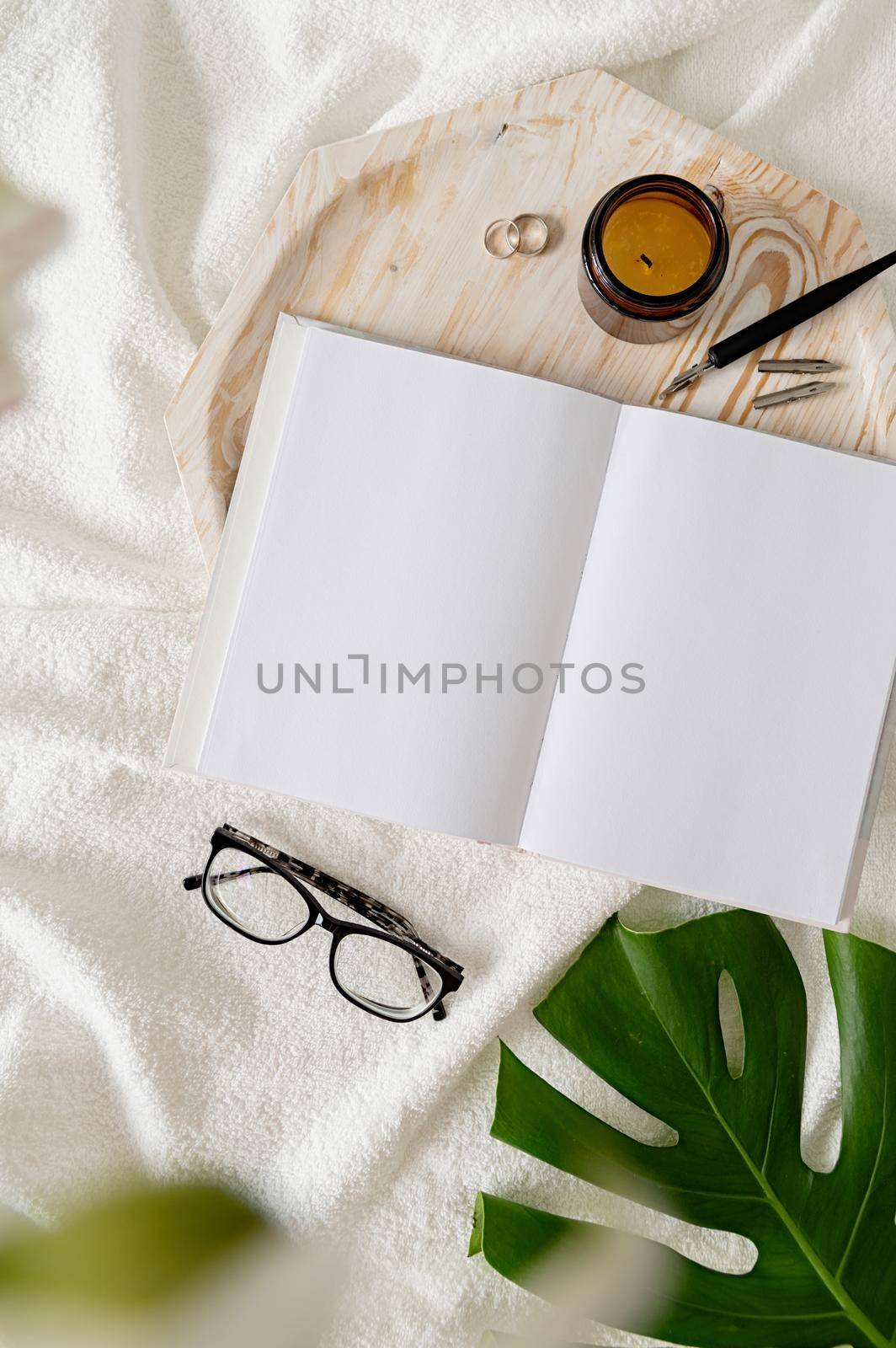 Blank opened book, candle, glasses, flowers on white bed, flat lay, mock up, flat lay