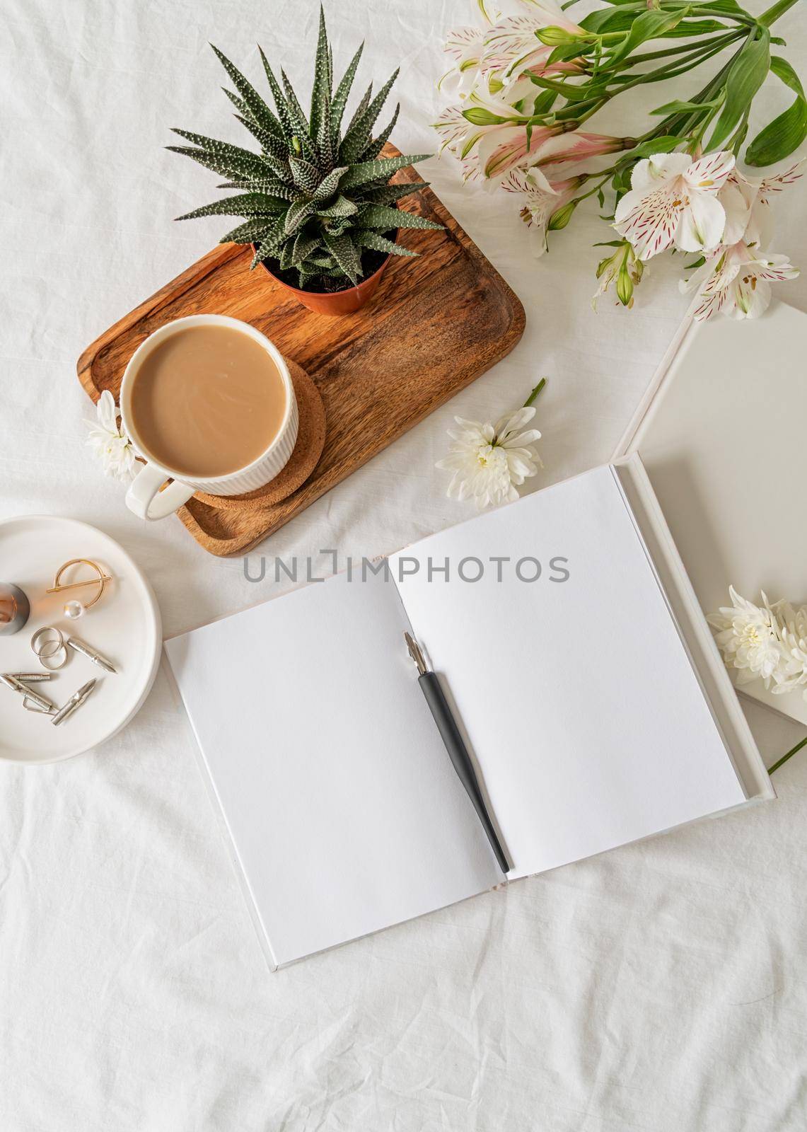 Opened book, coffee and flowers top view on white bed. Mock up design by Desperada