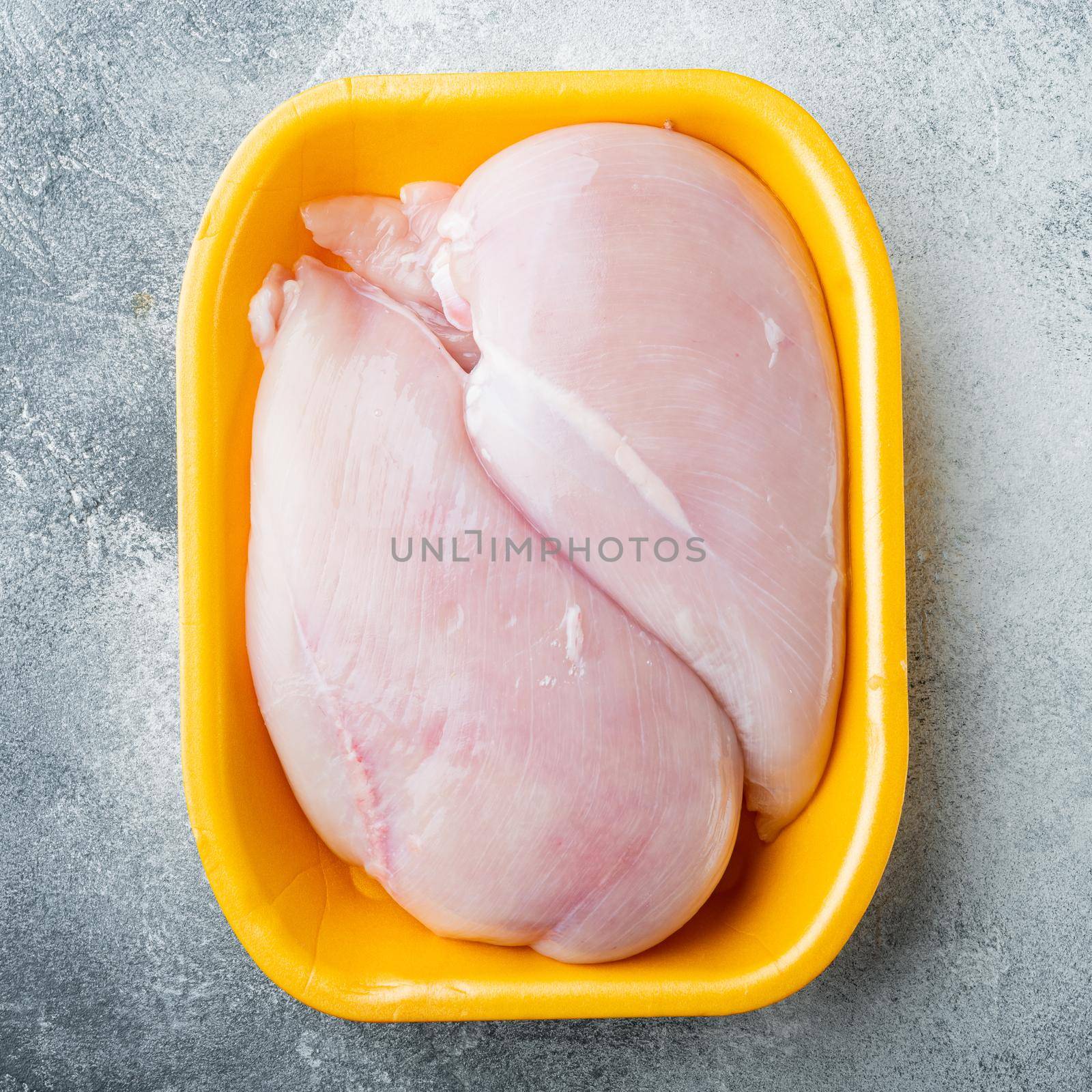 Fresh chicken breast meat in open tray, on gray background