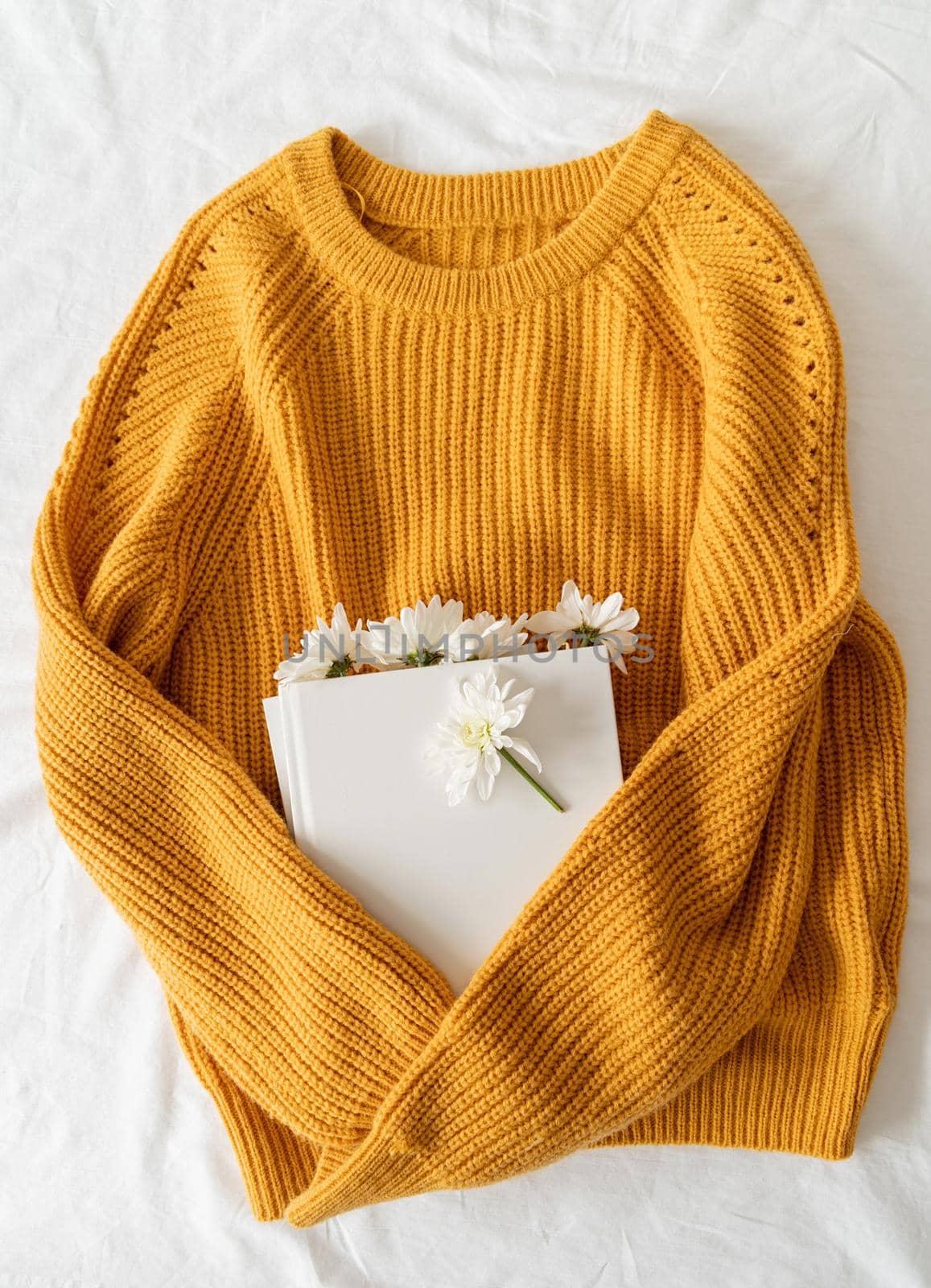 Top view of a book with white chrysanthemum flowers on yellow sweater by Desperada