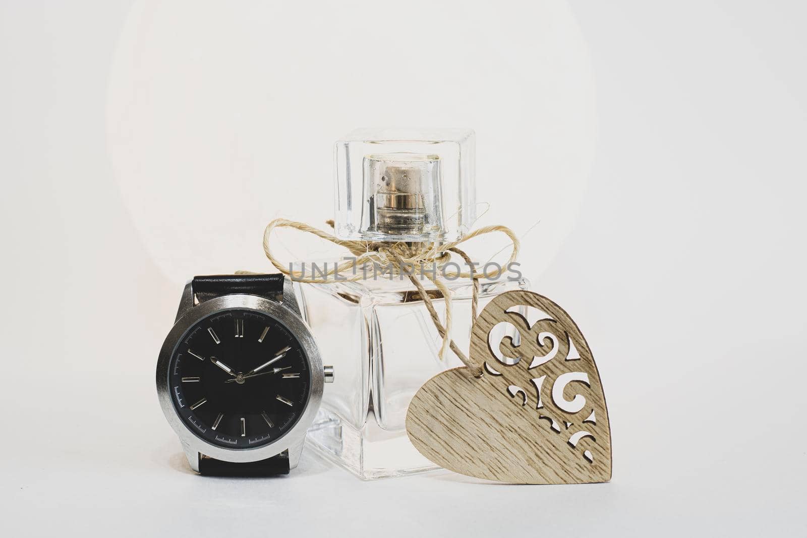 Women's perfume on a white background with a heart and a clock. Time to give gifts.