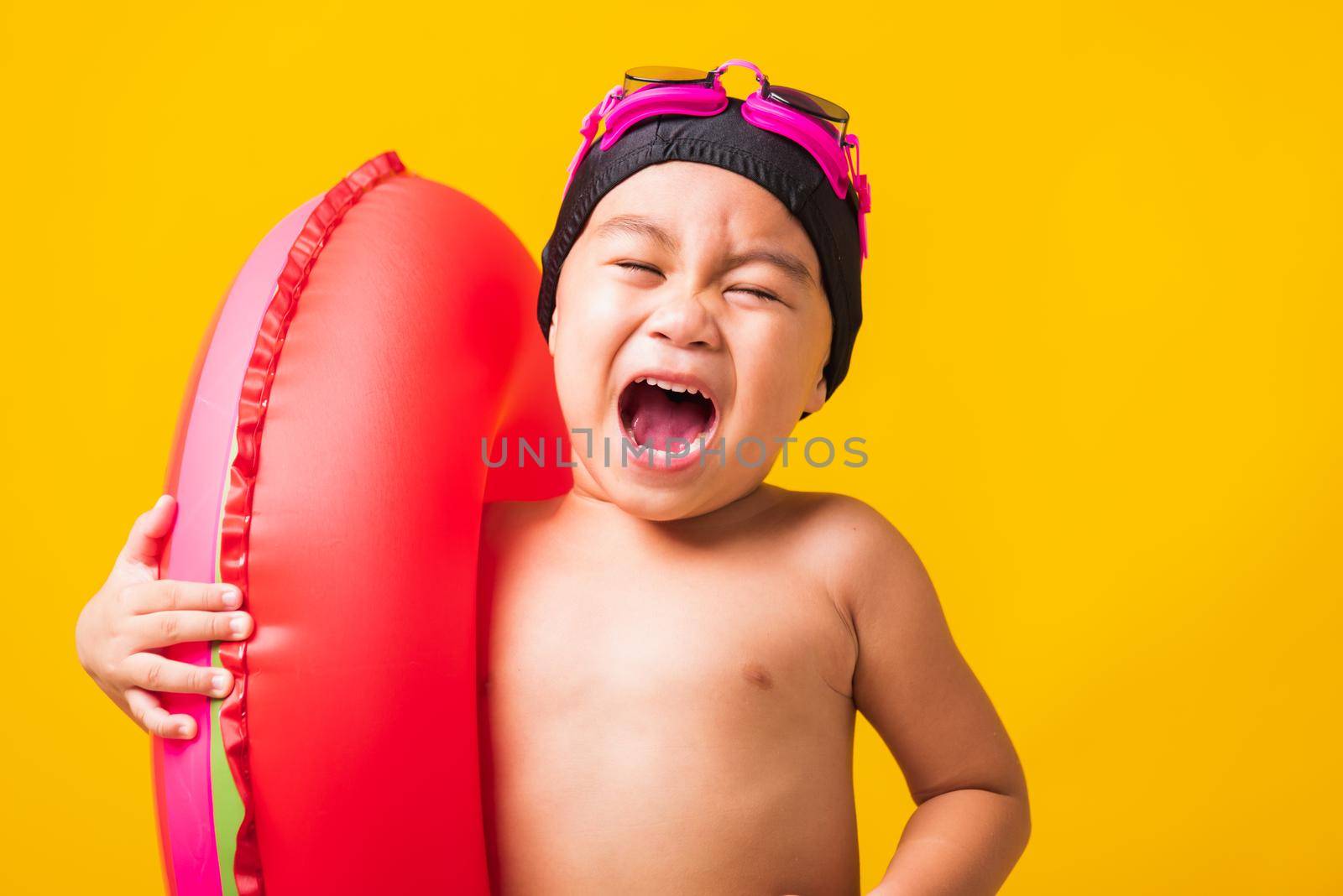 Summer vacation concept, Portrait Asian happy cute little child boy wear goggles and swimsuit hold watermelon inflatable ring, Kid having fun on summer vacation, studio shot isolated yellow background