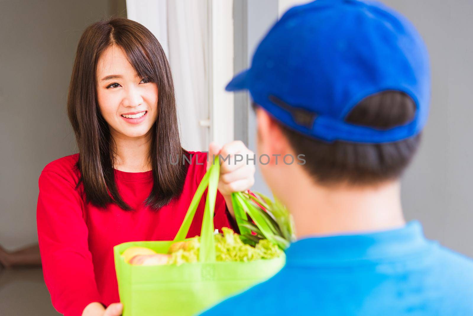 Delivery man making grocery service giving fresh vegetables and fruits and food in green cloth bag by Sorapop
