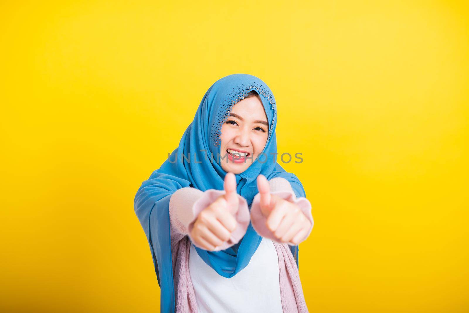 Asian Muslim Arab, Portrait of happy beautiful young woman Islam religious wear veil hijab funny smile she made finger thumbs up, Ok sign to agree, studio shot isolated on yellow background