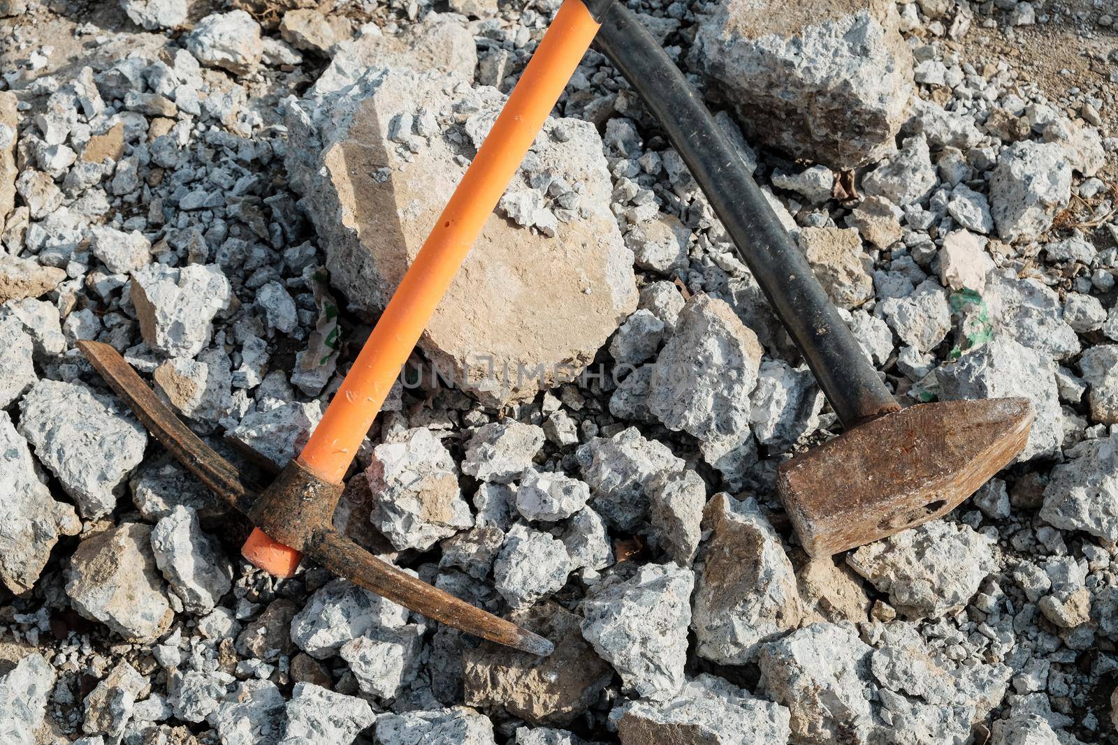 Geological pick with orange handle on the stones next to old hammer.