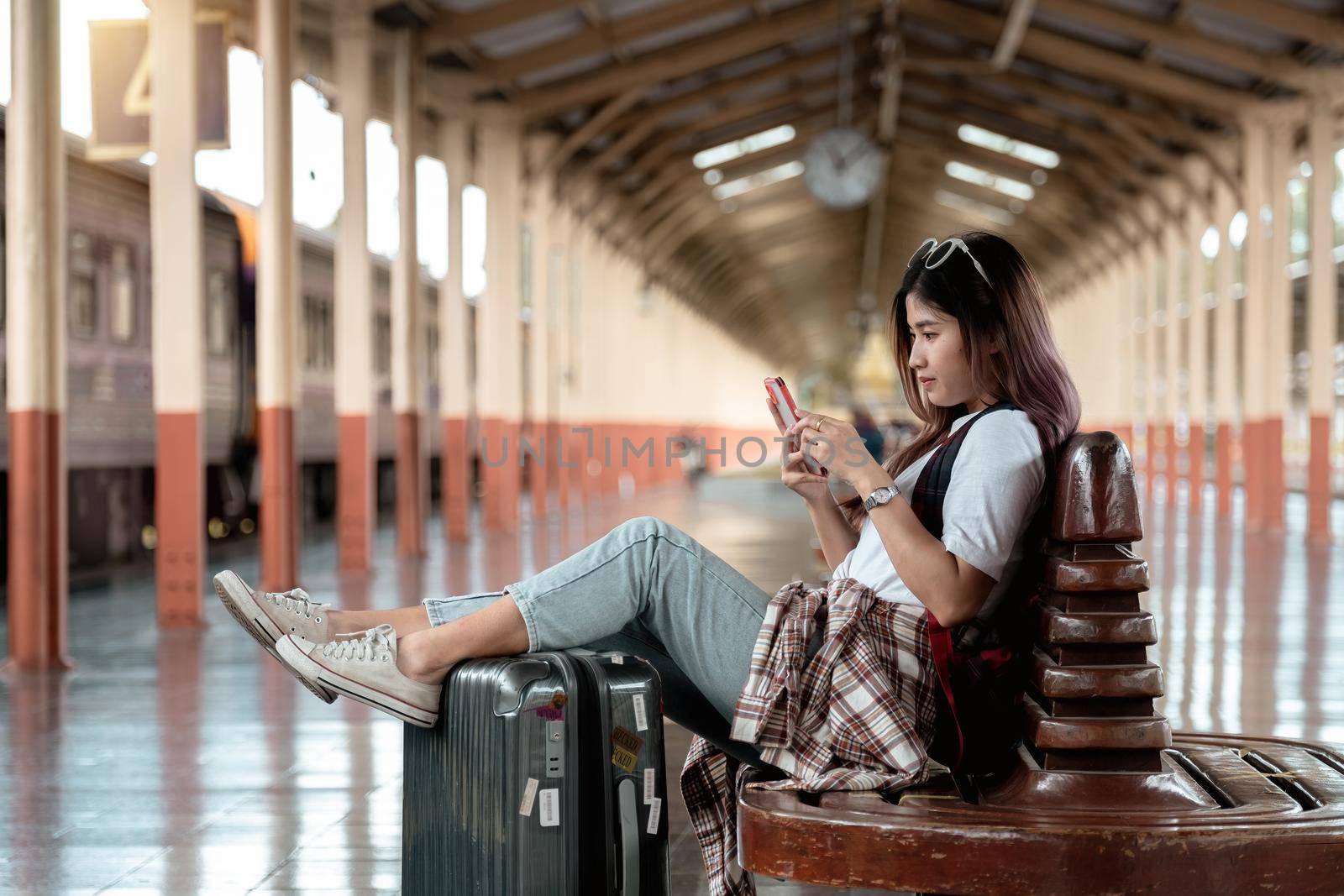 Asian woman is traveler, she is waiting for their train. Girl using smartphone at outdoor adventure travel by train concept.