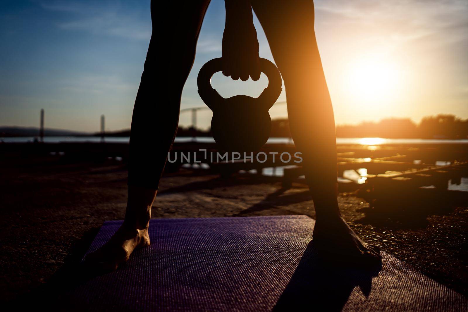 Woman exercising pilates with kettlebell in sunset.