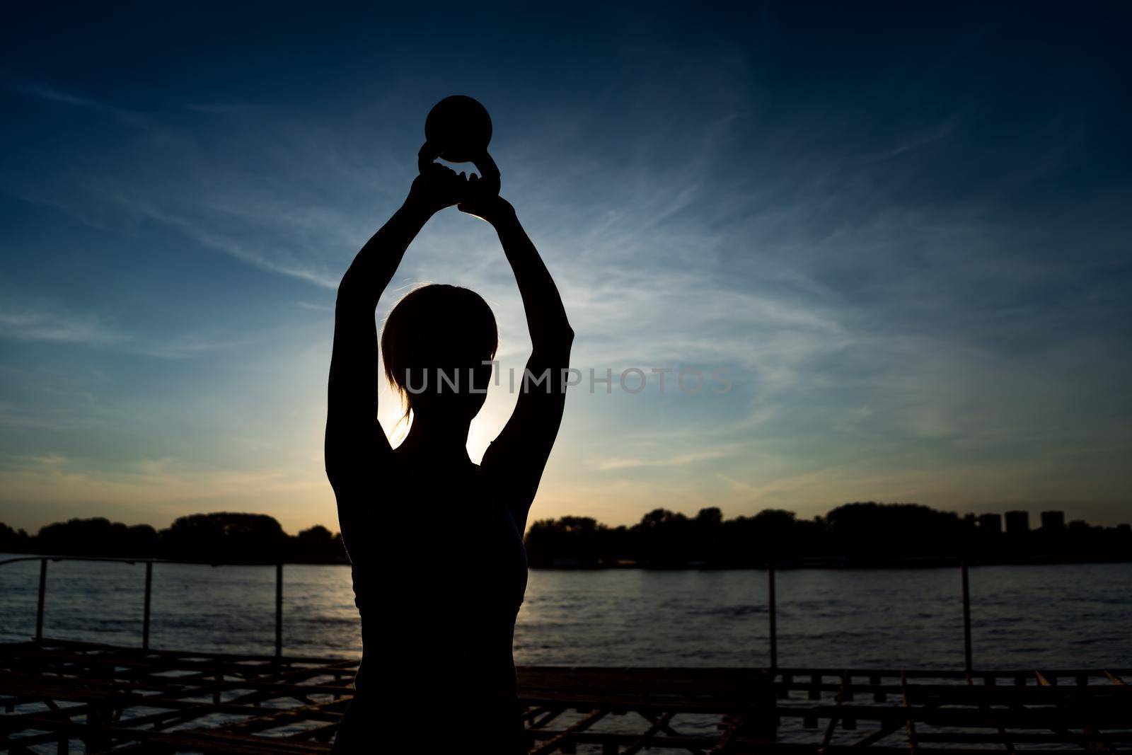 Woman exercising pilates with kettlebell in sunset.