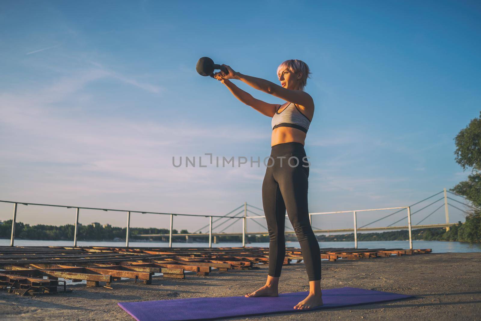Woman practicing kettlebell pilates on sunny day.