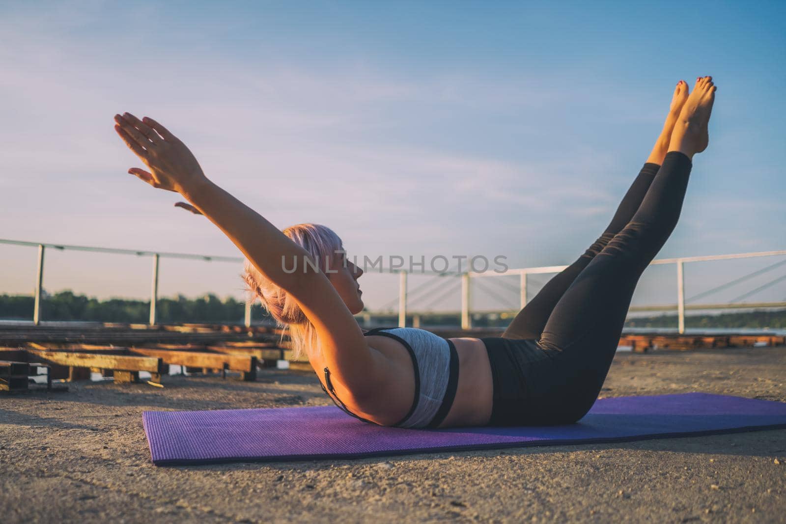 Woman exercising pilates on sunny day. Double leg stretch exercise.