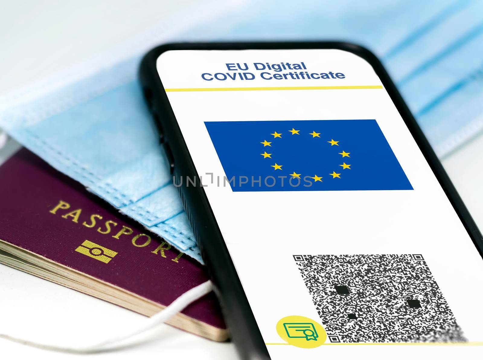 EU Digital COVID Certificate with the QR code on the screen of a mobile phone over a surgical mask and a passport. Immunity from Covid-19. Travel without restrictions.