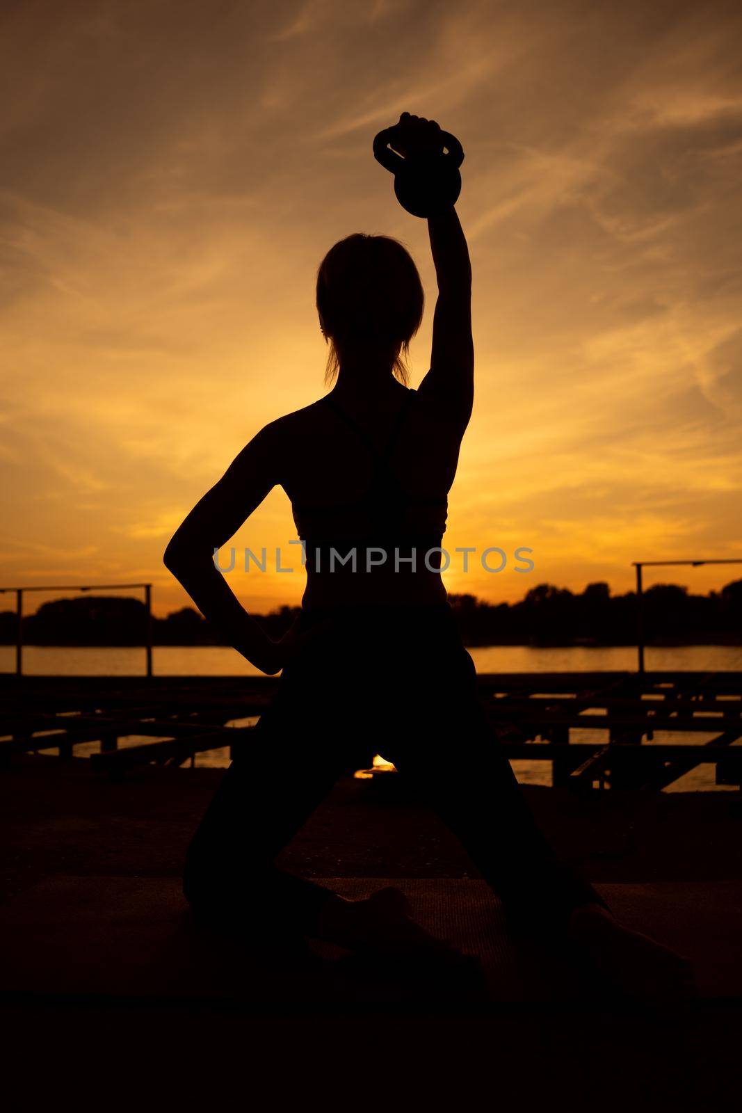Woman exercising pilates with kettlebell in sunset.