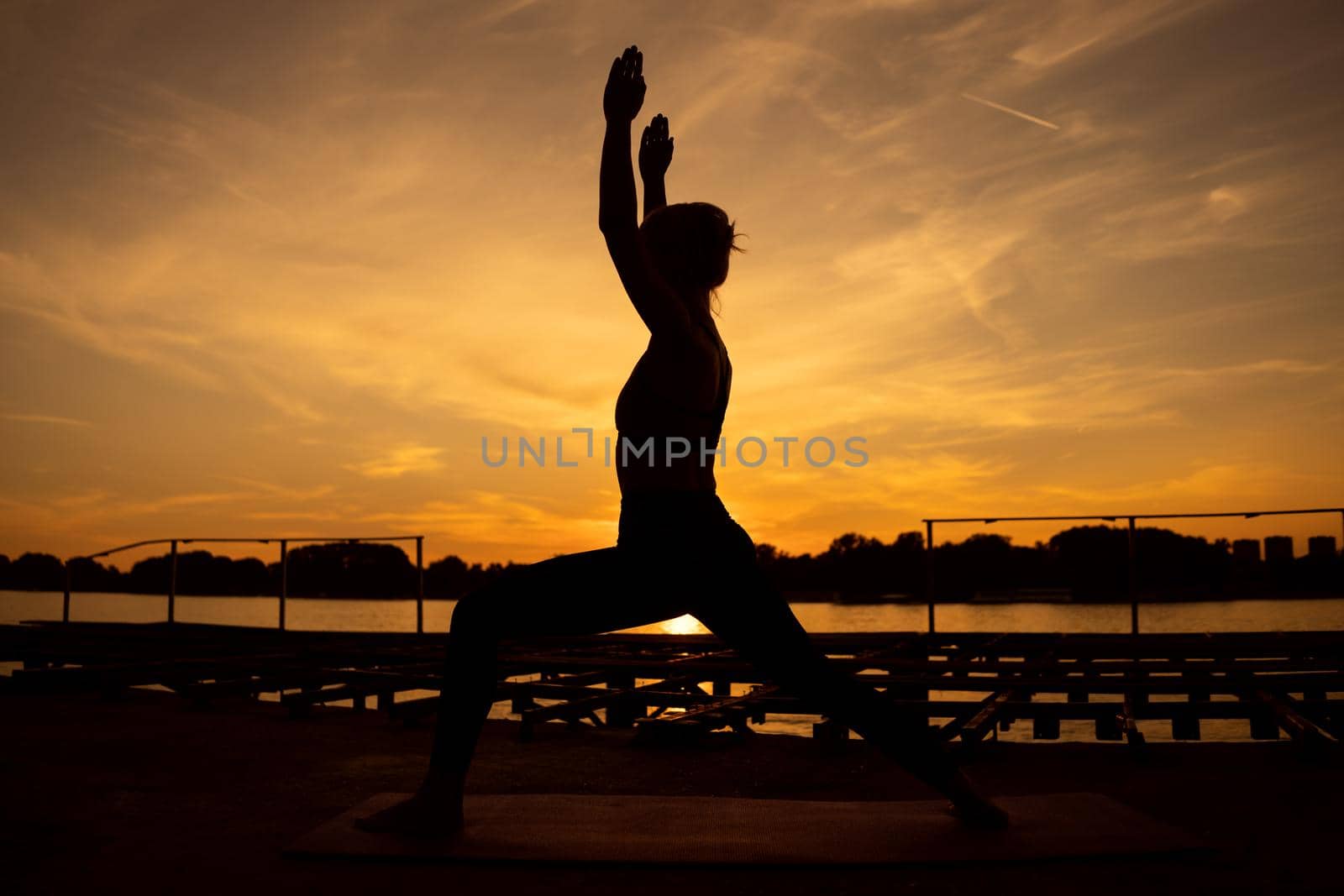 Woman practicing yoga in sunset. Virabhadrasana / Warrior pose