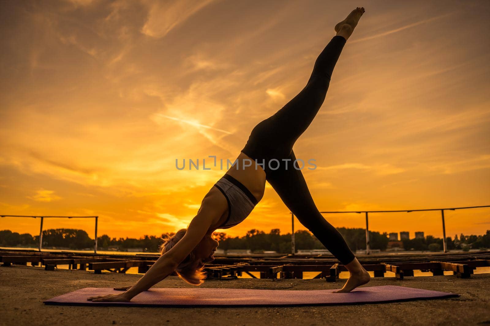 Woman practicing yoga in sunset. Eka Pada Adho Mukha Svanasana/One-Legged Downward-Facing Dog Pose