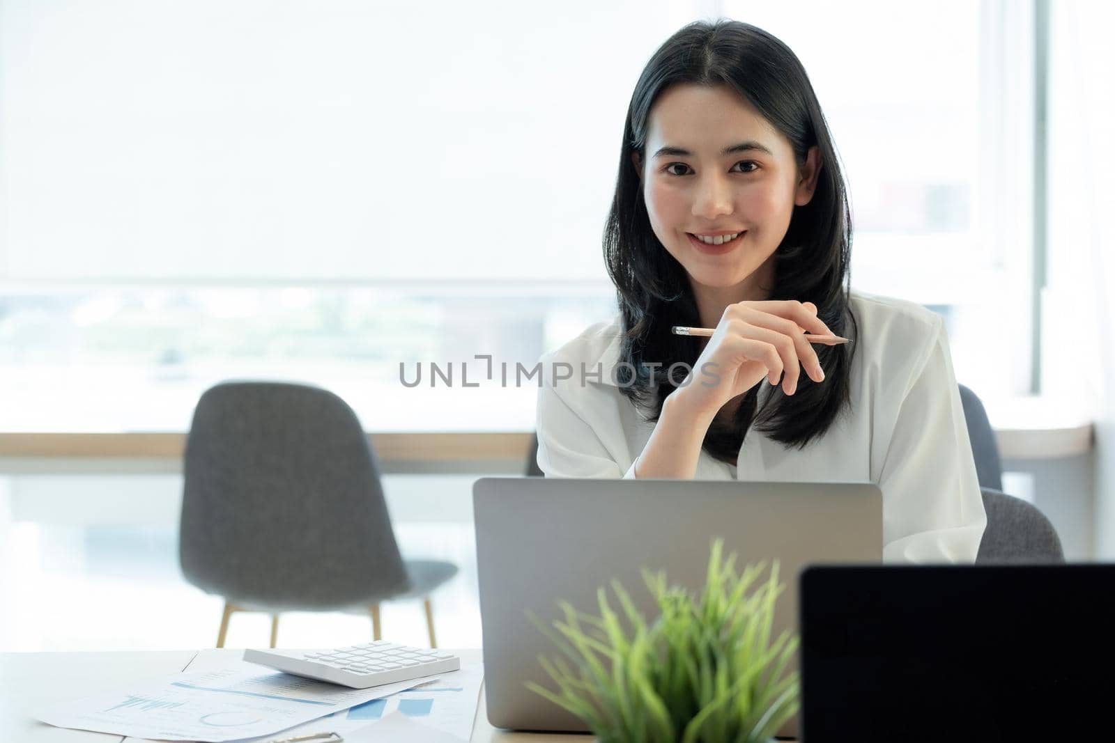 Happy young asian girl working at a her office with a laptop and calculator. Portrait of businesswoman look at camera.