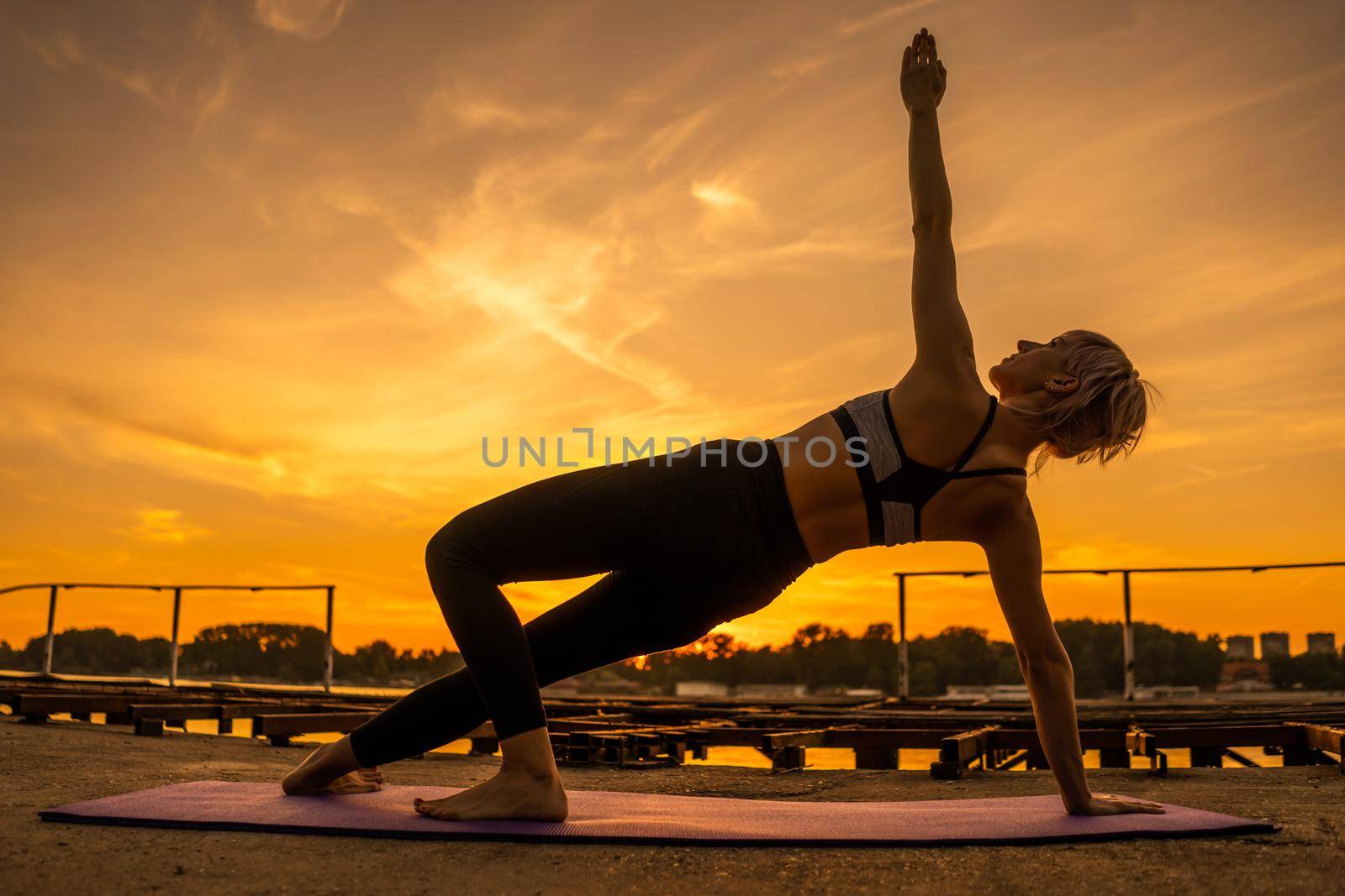 Woman exercising pilates in sunset. Side plank exercise.