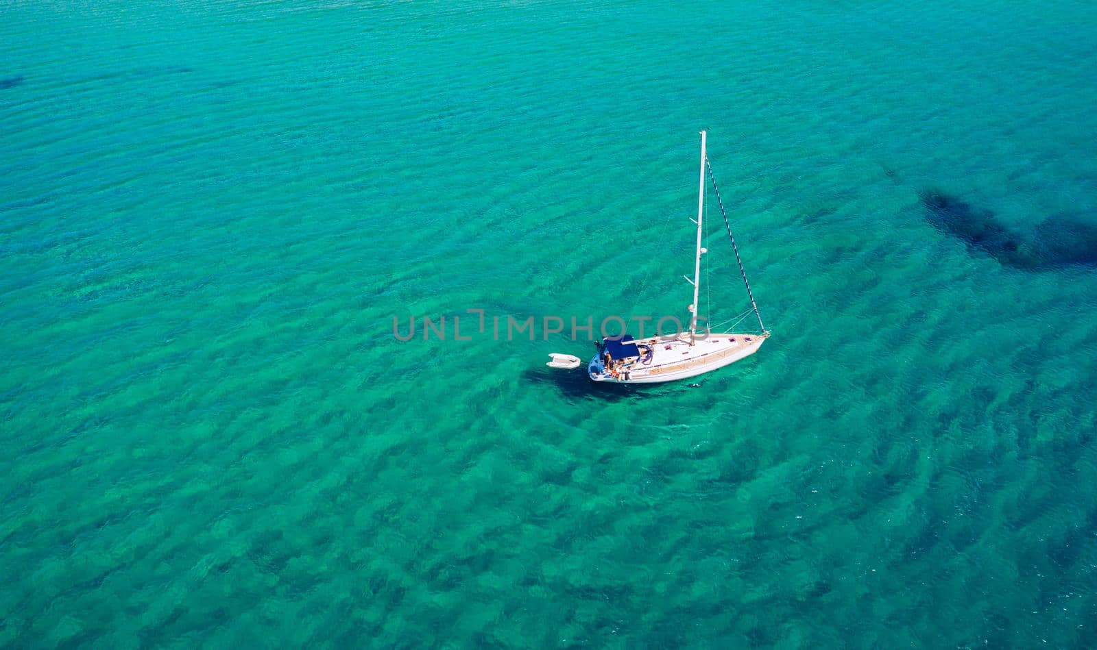 Aerial view of anchored sailing yacht in emerald sea. Aerial view of a boat. Outdoor water sports, yachting. Aerial view of anchoring yacht in open water. Ocean and sea travel and transportation