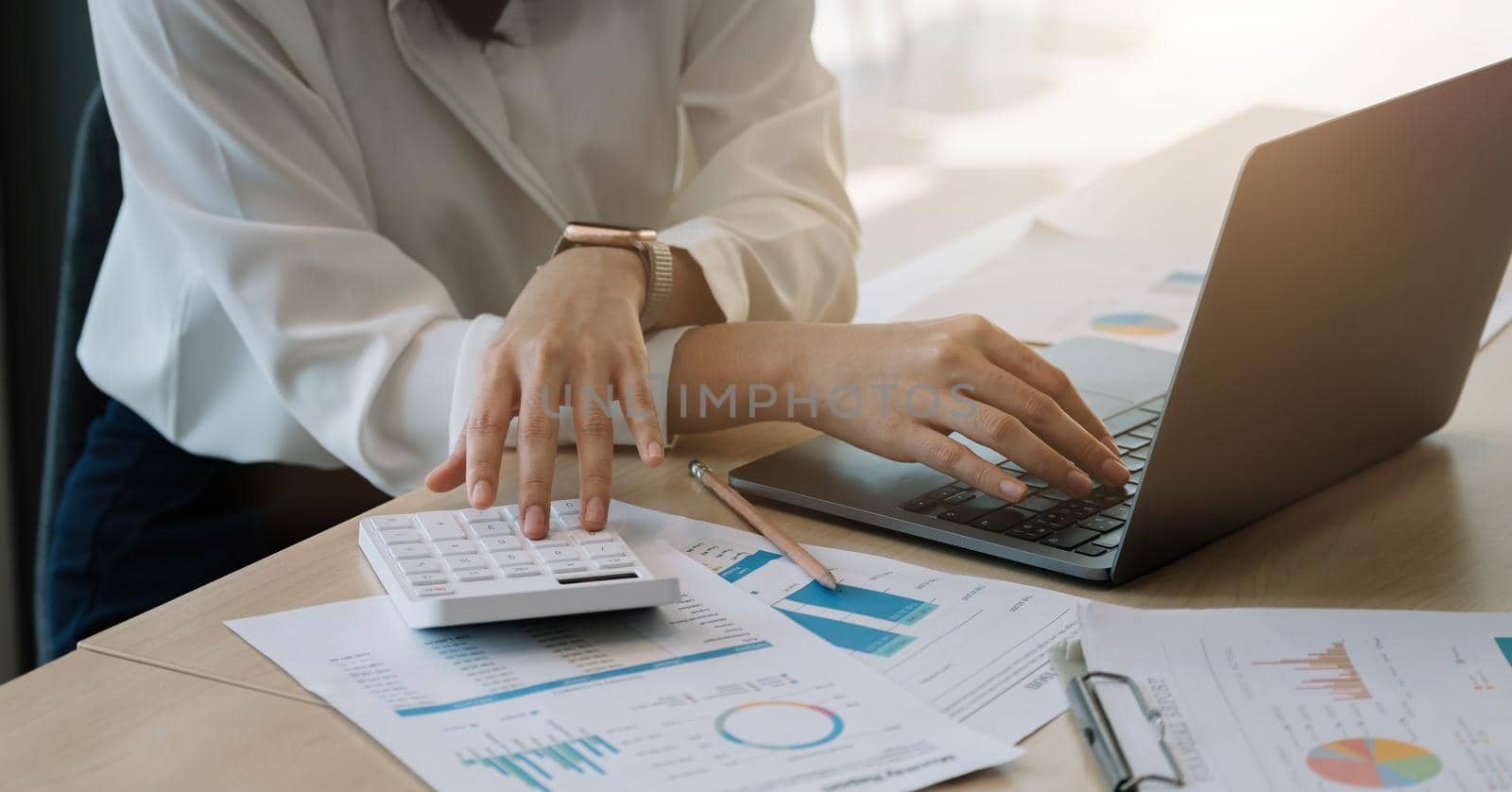 Close up of businesswoman or accountant hand holding pencil working on calculator to calculate financial data report, accountancy document and laptop computer at office, business concept.