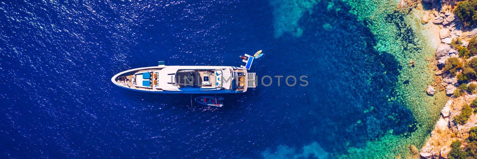 Aerial view of anchored sailing yacht in emerald sea. Aerial view of a boat. Outdoor water sports, yachting. Aerial view of anchoring yacht in open water. Ocean and sea travel and transportation