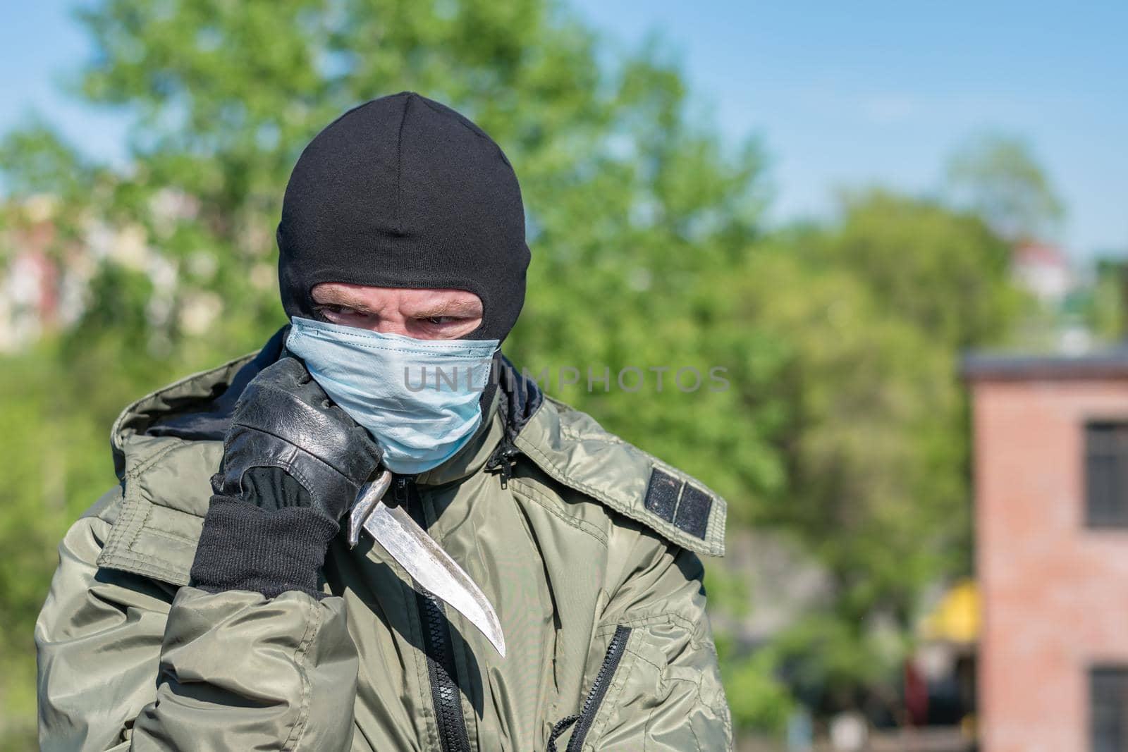 Pensive soldier in balaclava and medical mask with a knife in his hands