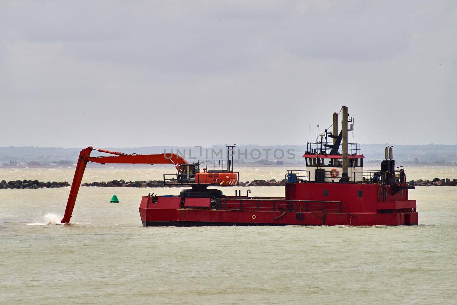 The arm of an excavator on a dredging ship digs sand and mud from the seabed in port