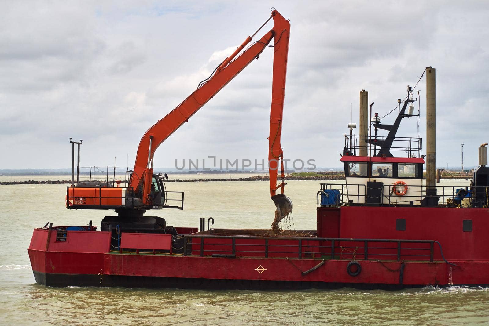 An excavator loads sand into a dredger by ChrisWestPhoto