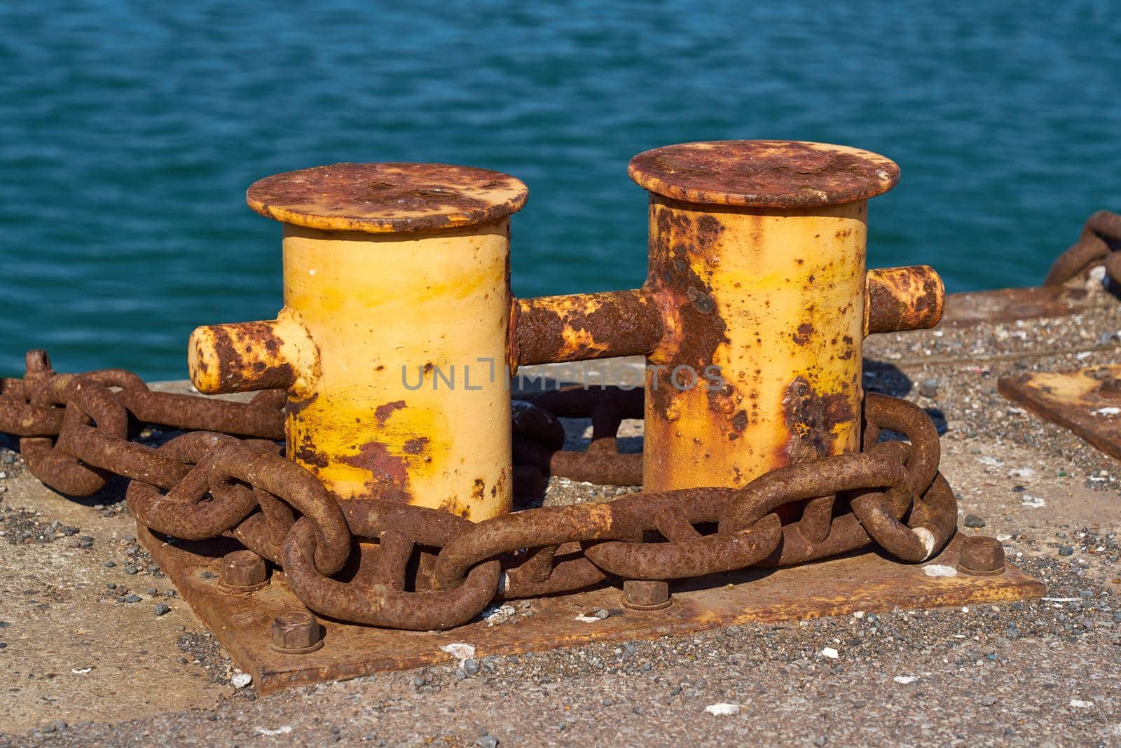 Side View of A double bitt mooring bollard with a heavy chain around it. by ChrisWestPhoto