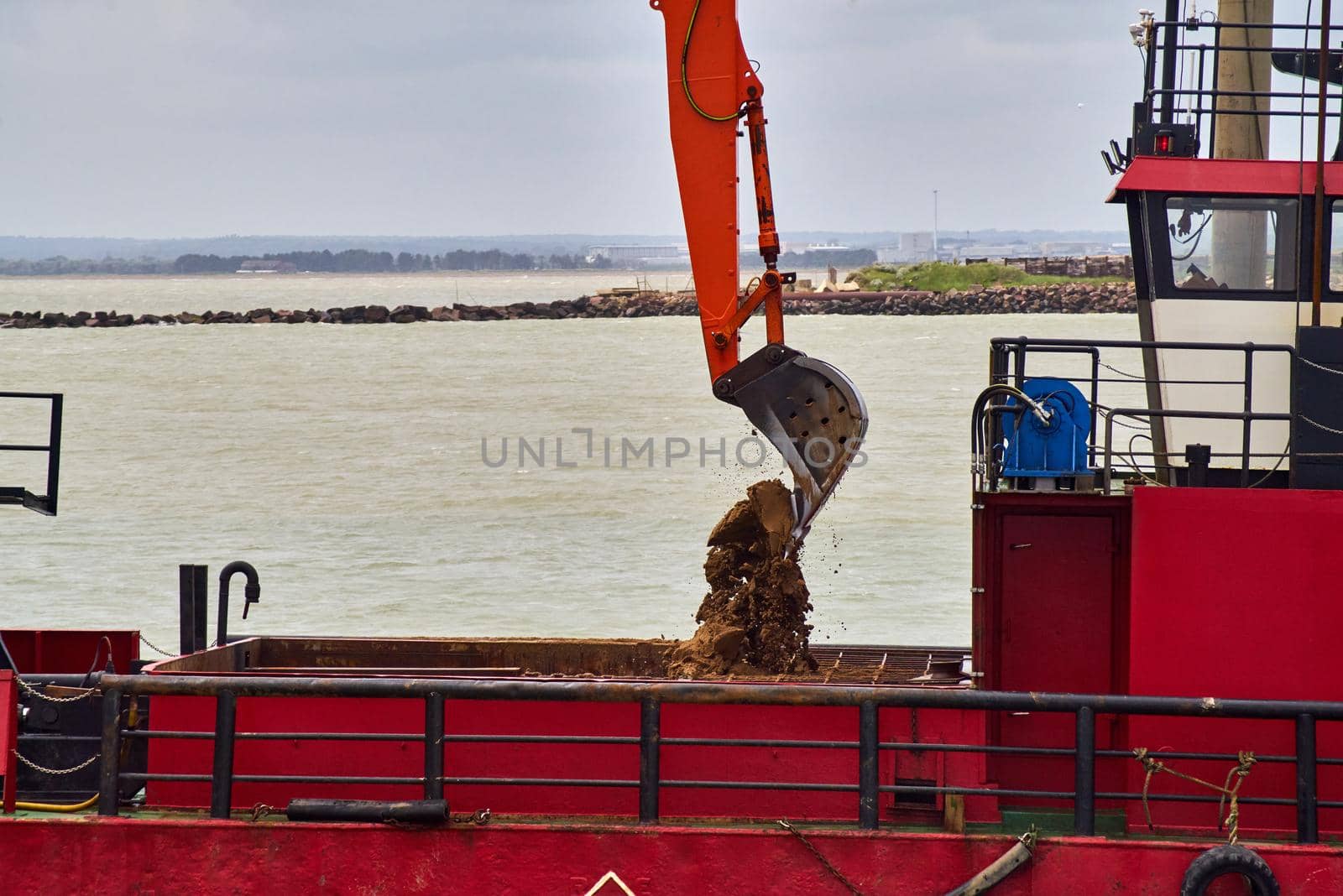 Mud and sand falls from the bucket of an excavator into a dredging ship