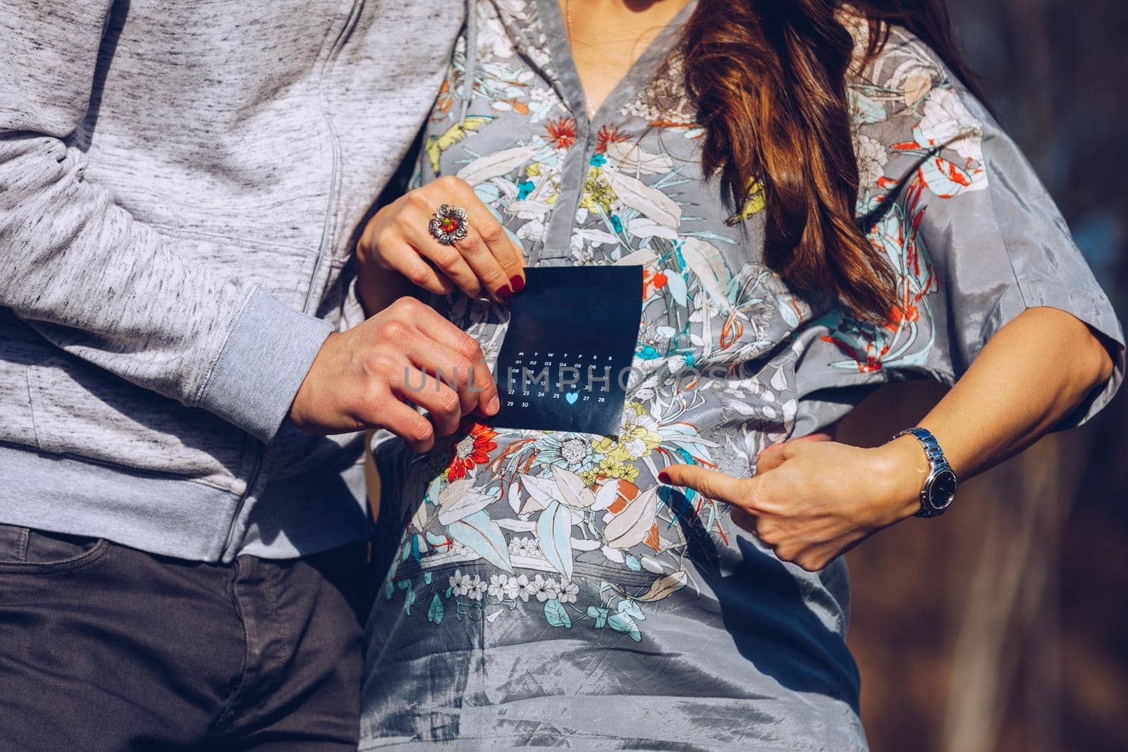 Young pregnant couple marking child birth day in calendar. Baby expecting concept. Planning of future. Adult man and pregnant woman demonstrating calendar and pointing at calendar baby birth date