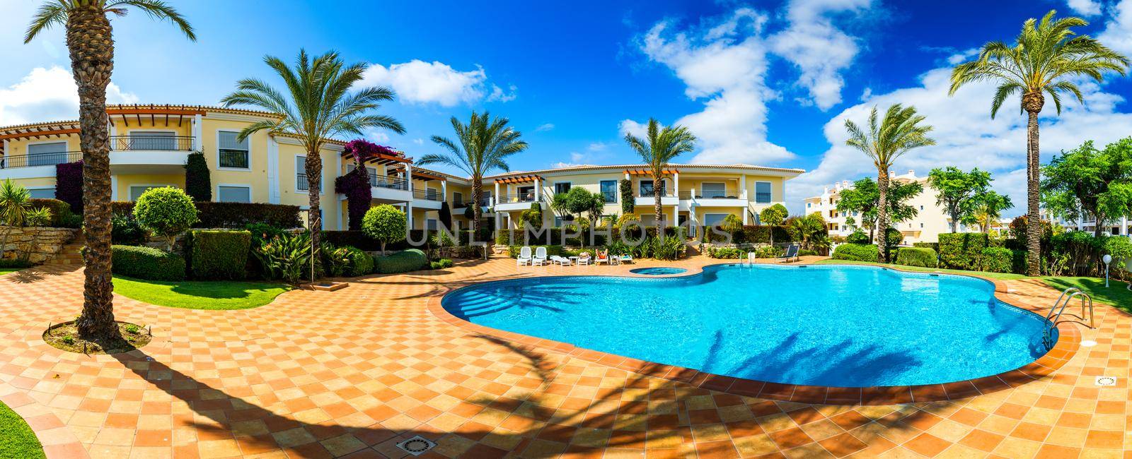 Swimming pool, sun-loungers and palm trees during a warm sunny day, paradise destination for vacations. Backyard swimming pool with garden full of palm trees and flowers. Backyard with swimming pool.