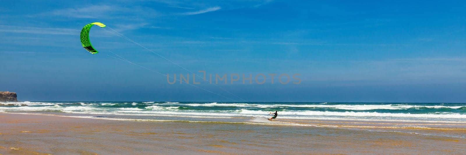 Surfers in Praia da Bordeira beach near Carrapateira, Portugal. Kiteboarder kitesurfer athlete performing kitesurfing kiteboarding tricks. Praia da Bordeira is popular location for surfing. Portugal