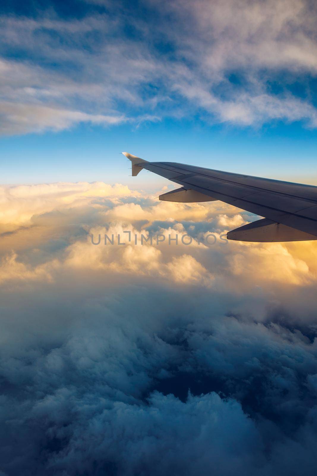 Flying and traveling, view from airplane window on the wing on sunset time. Aircraft wing under the earth and clouds. Flight in sky. Looking over aircraft wing in flight. 
