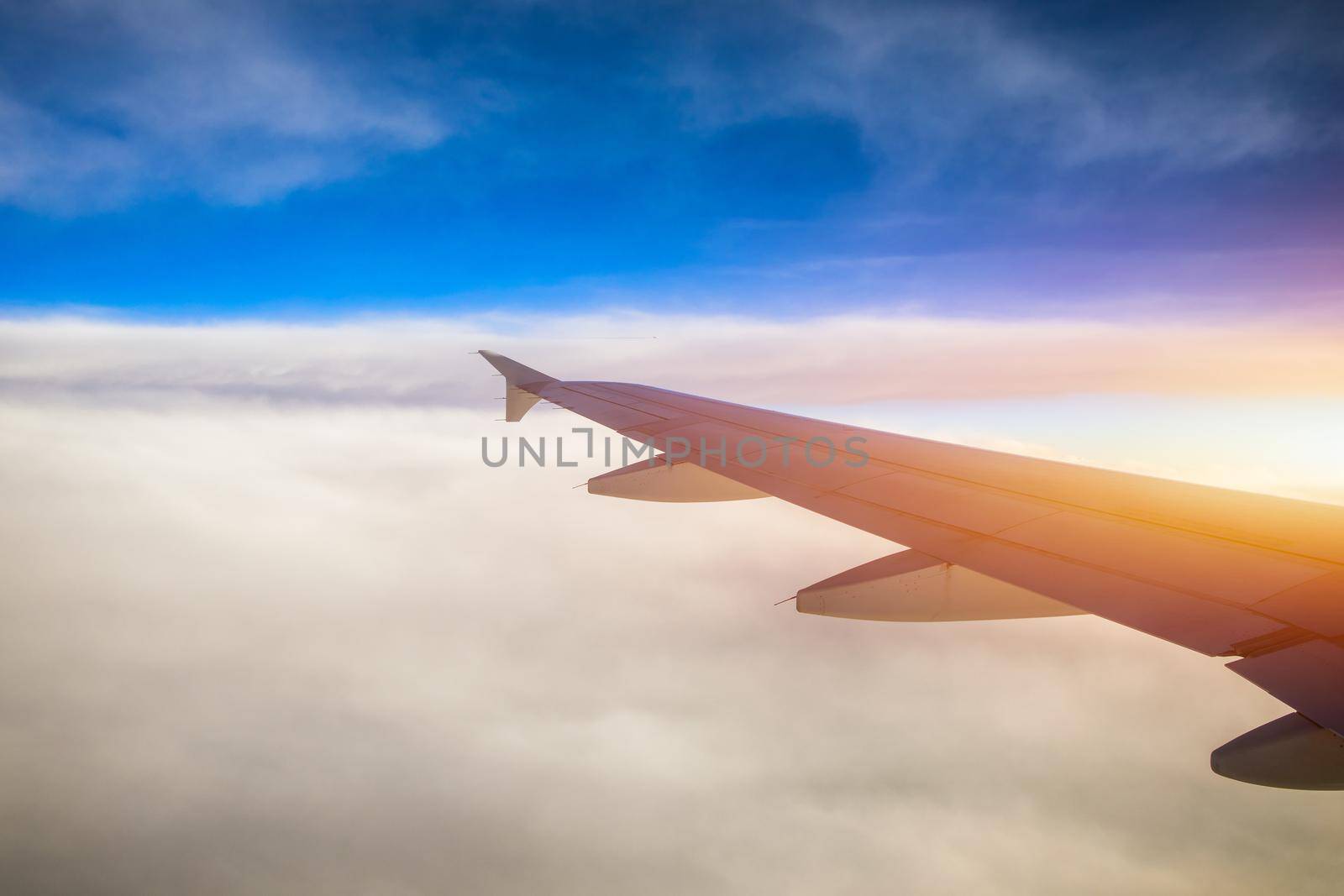 Flying and traveling, view from airplane window on the wing on sunset time. Aircraft wing under the earth and clouds. Flight in sky. Looking over aircraft wing in flight. 
