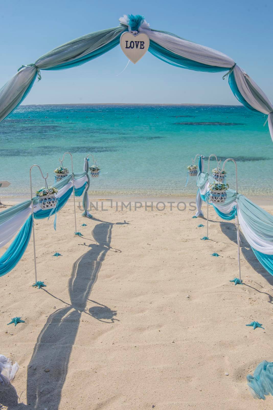Setup of wedding day marriage aisle with drapes and arch on sandy tropical beach paradise to open ocean background 