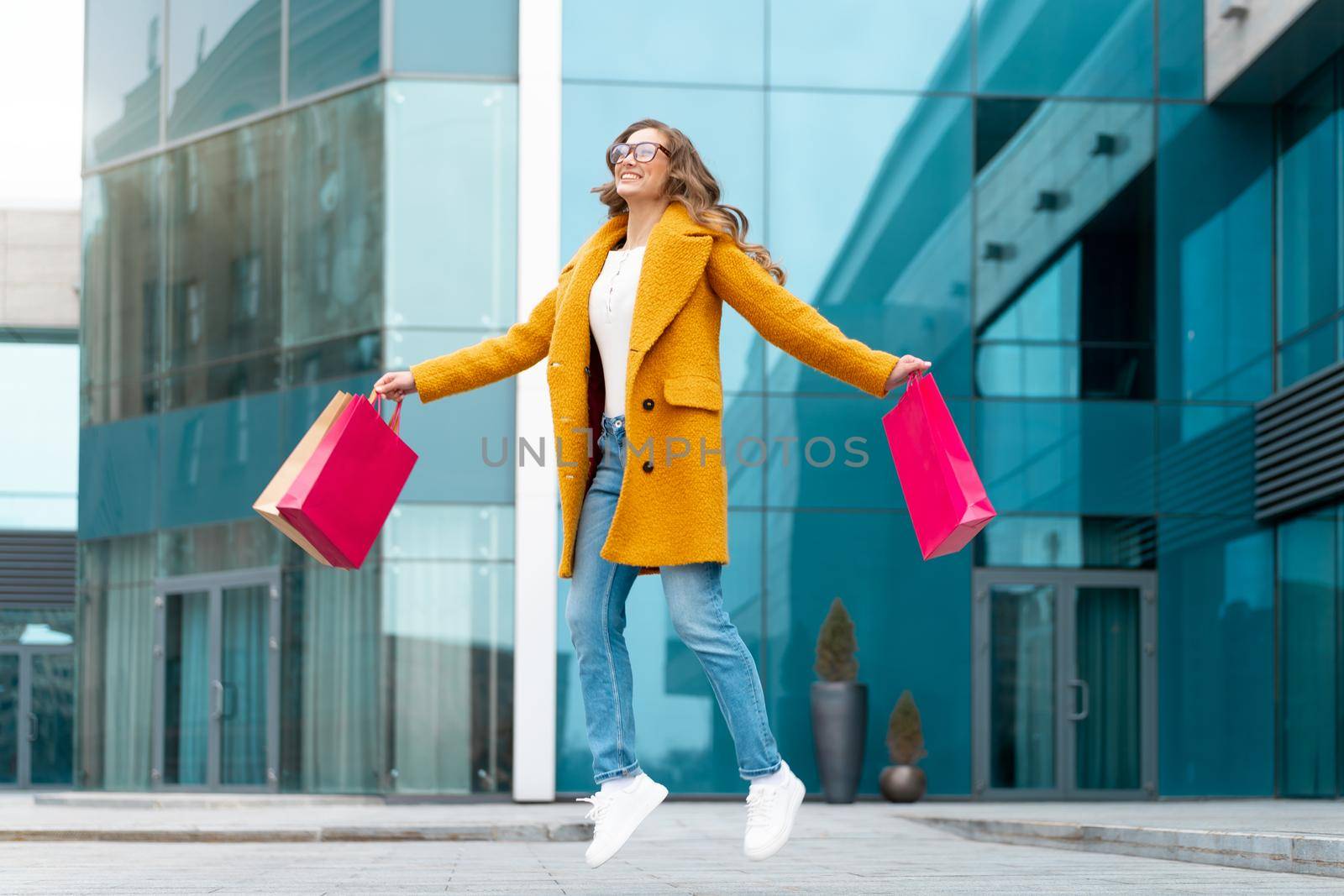 Business Woman With Shopping Bags Dressed Yellow Coat Jumping With Happiness Outdoors Corporative Building Caucasian Female Business Person Near Office Building Stylish Businesswoman Season Sale