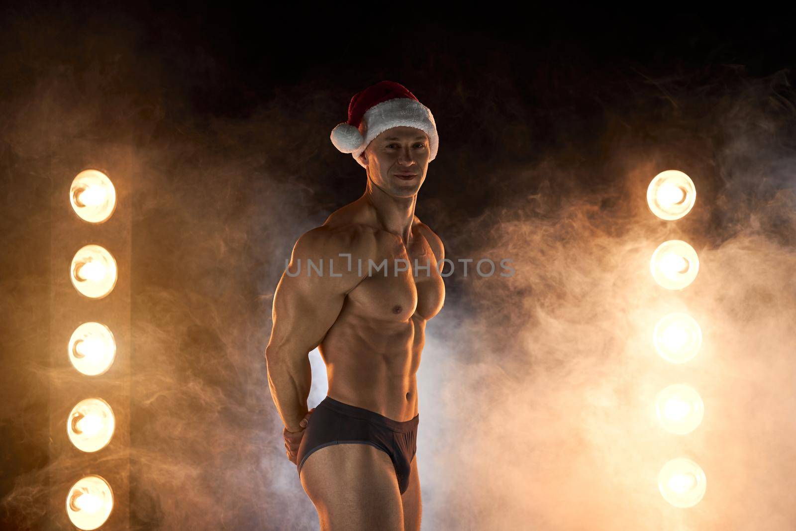 Portrait of muscular man wearing Christmas Santa hat, standing athletic pose on smoky background Macho Shirtless Naked torso stripper Hot sexy Santa guy Seductive male for holiday