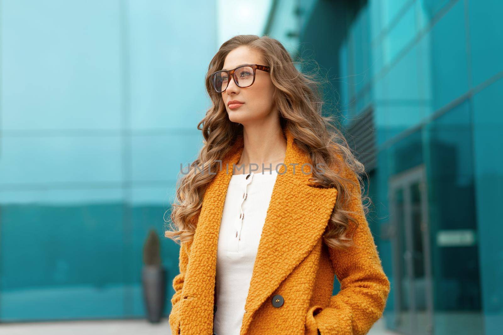 Business woman dressed yellow coat standing outdoors corporative building background Caucasian female business person eyeglasses on city street near office building big windows Stylish businesswoman