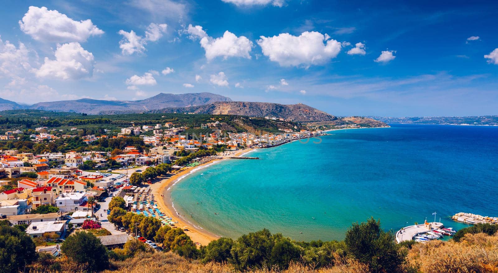 Greek holidays, beautiful Kalyves village with turquoise sea in Crete island, Greece. View of Kalyves beach, Crete. Tourists relaxing on the beach and views to the mountains, Kalyves, Crete, Greece
