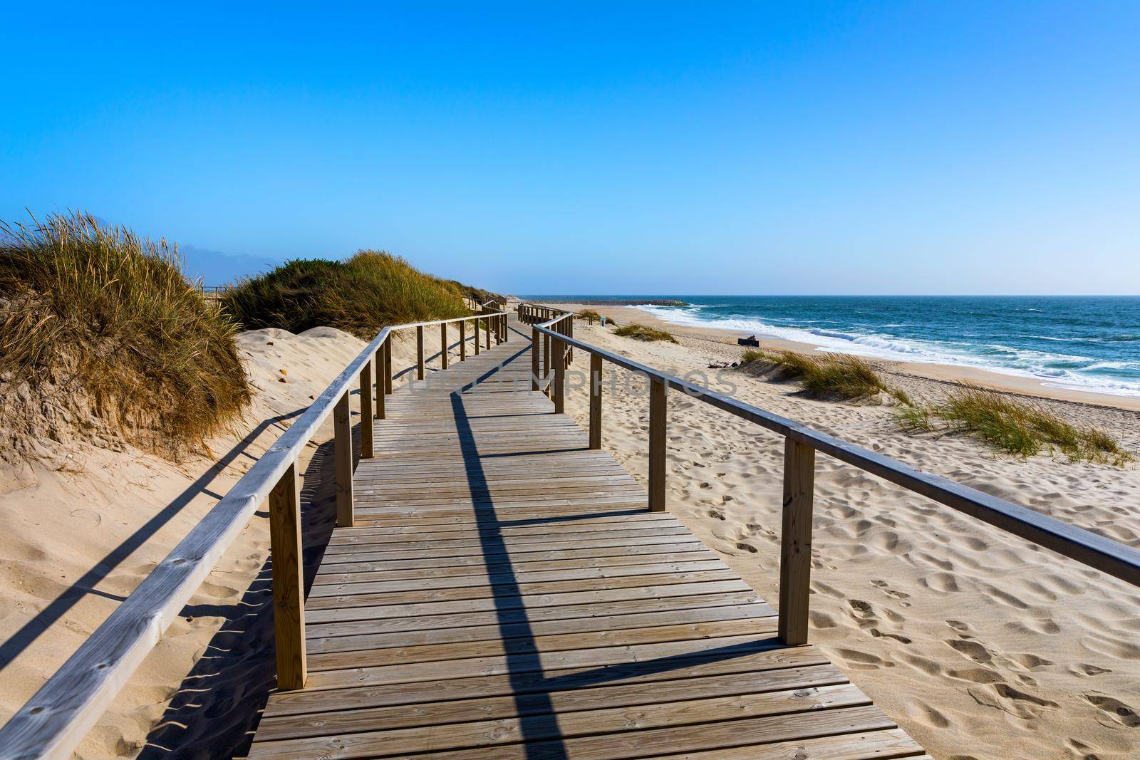Wooden path at Costa Nova d'Aveiro, Portugal, over sand dunes with ocean view, summer evening. Wooden footbridge of Costa Nova beach in a sunny day. Aveiro, Portugal. 