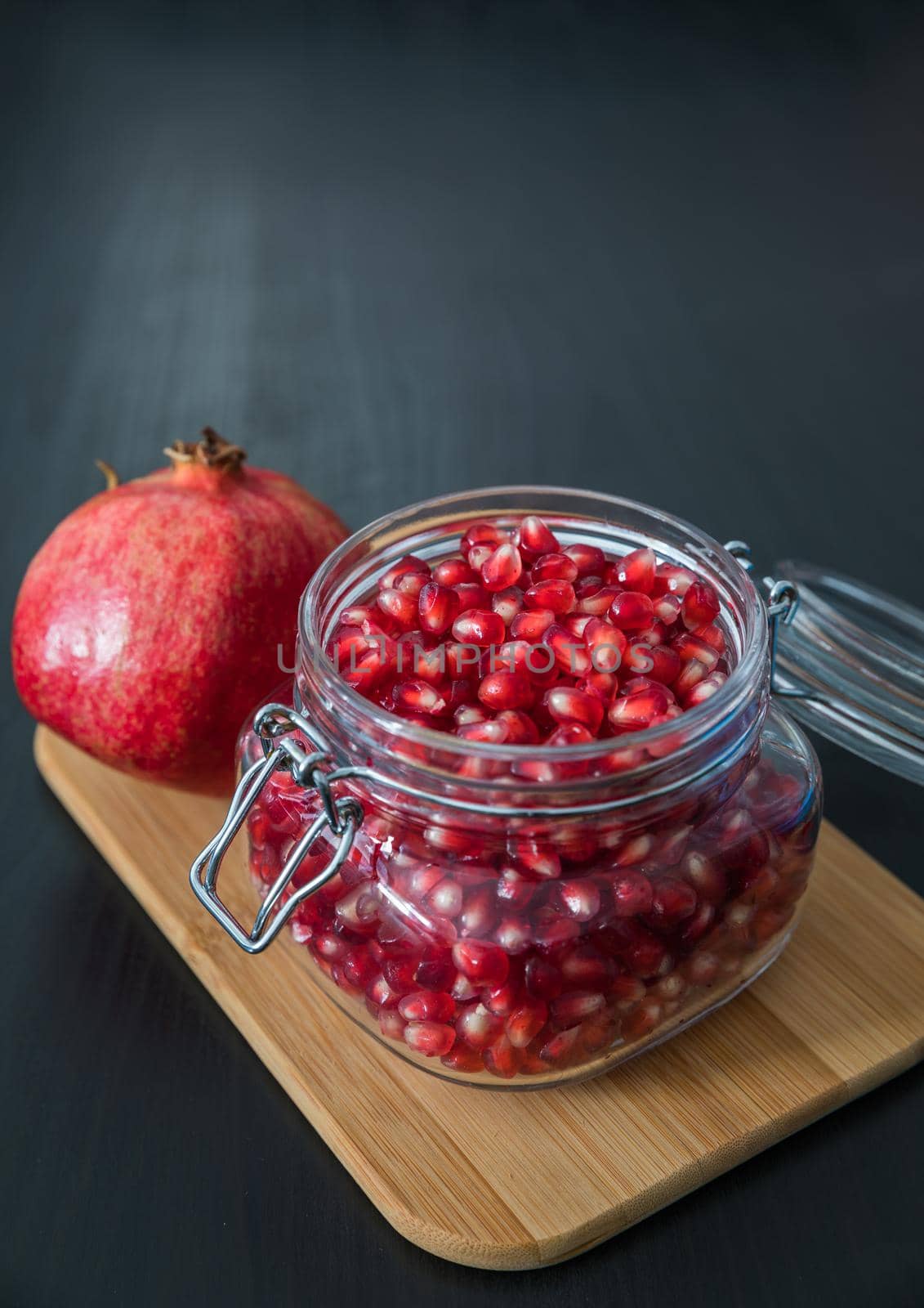 Delicious pomegranate seeds placed in glass jar with fresh organic pomegranates on rustic wooden background.Close up,Copy space