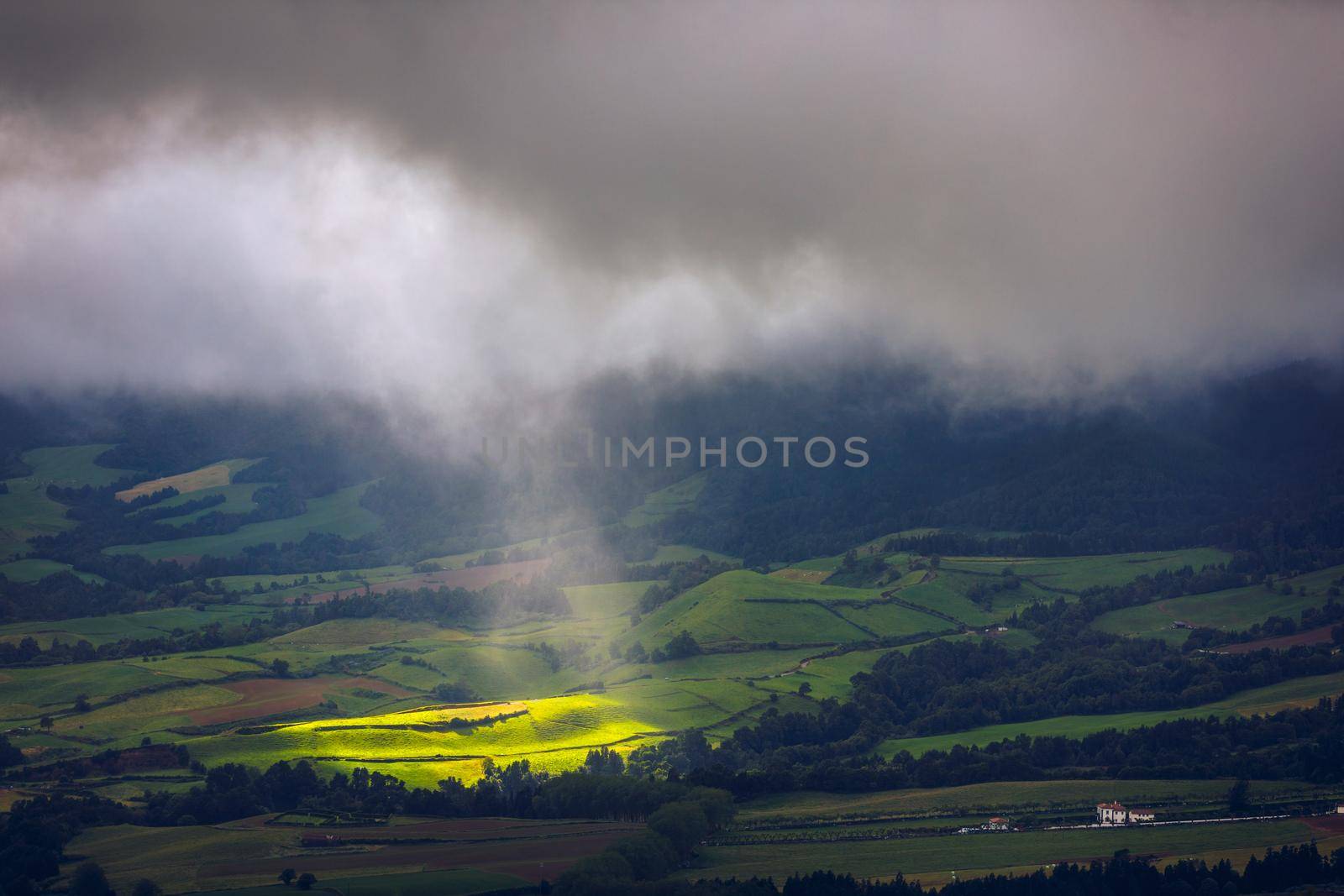 Bright sunlight shining through hole of clouds to dark scene of mountain range, Azores, Sao Miguel, Portugal. The beam of light through the dark clouds on the mountains in Azores, Portugal.