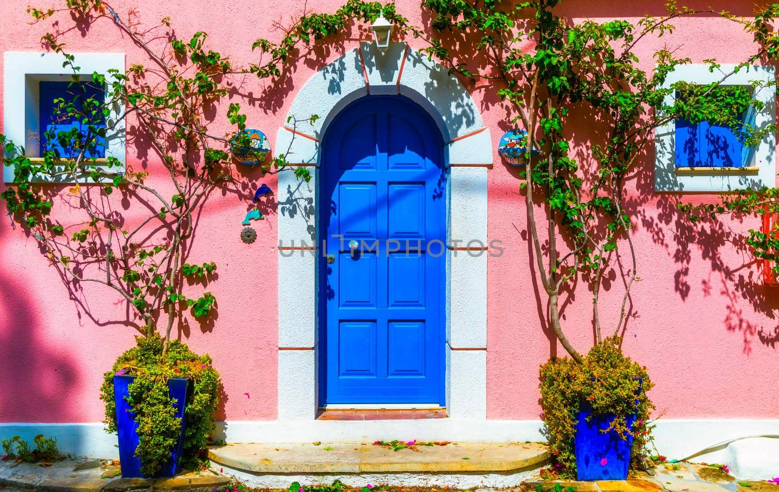 Traditional street with greek houses with flowers in Assos, Kefalonia island. Traditional colorful greek houses in Assos village. Blooming fuchsia plant flowers. Kefalonia island, Greece