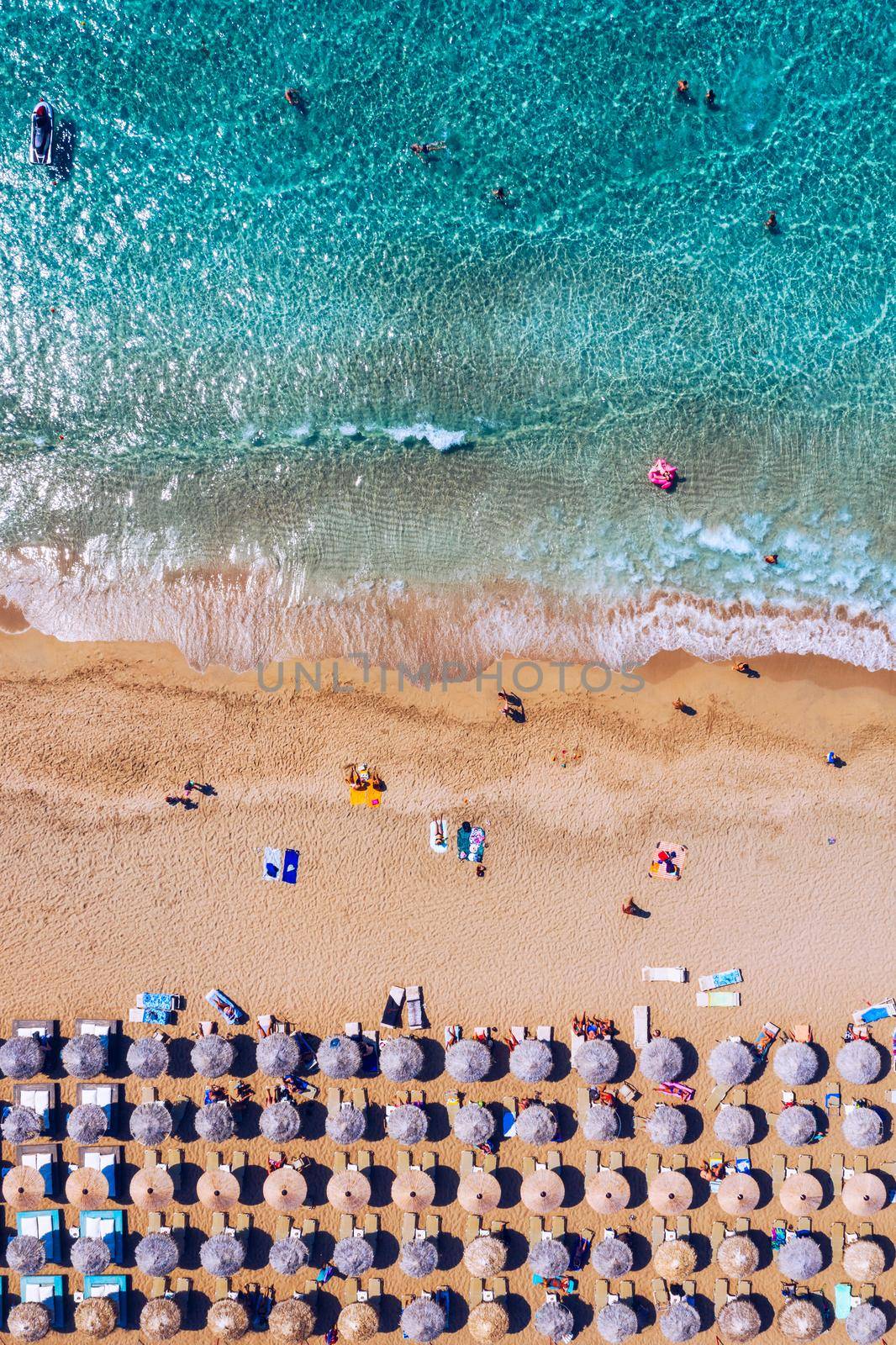 Aerial view of sandy beach with colorful umbrellas, swimming people in sea bay with transparent blue water at sunset in summer. Aerial top view on the beach, umbrellas, sand and sea waves.