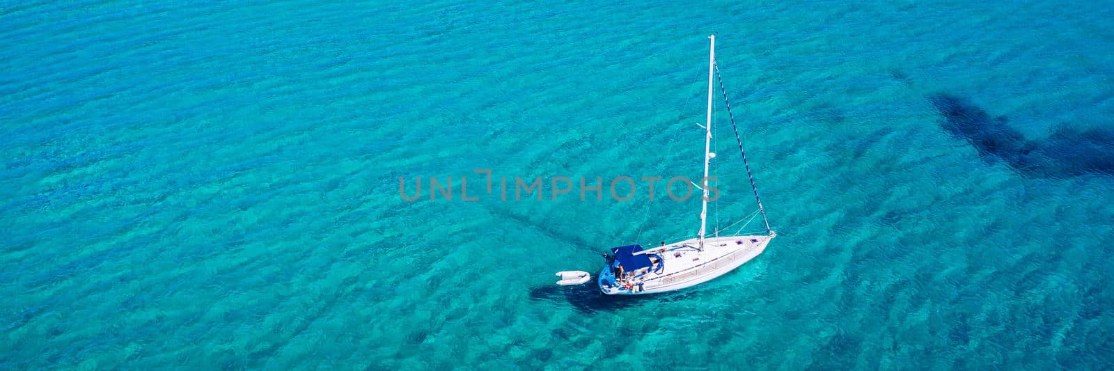 Yacht anchoring in crystal clear turquoise water in front of the tropical island, alternative lifestyle, living on a boat. Aerial view of yacht at anchor on turquoise water, showing luxury, wealth.