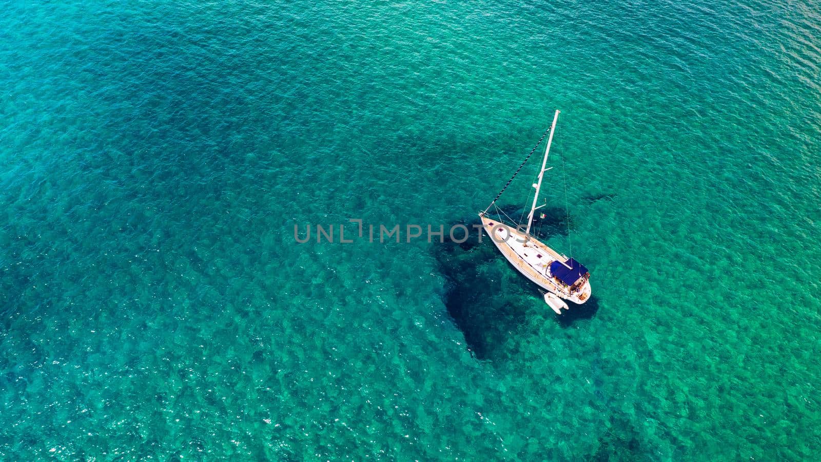 Yacht anchoring in crystal clear turquoise water in front of the tropical island, alternative lifestyle, living on a boat. Aerial view of yacht at anchor on turquoise water, showing luxury, wealth.