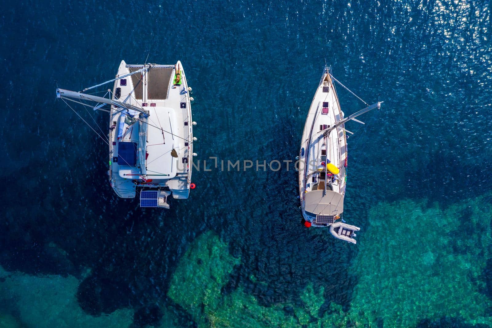 Aerial view of anchored sailing yacht in emerald sea. Aerial view of a boat. Outdoor water sports, yachting. Aerial view of anchoring yacht in open water. Ocean and sea travel and transportation